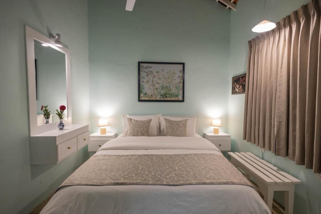 A bedroom with a bed, bedside tables, a mirror, a framed picture, and a window with curtains.