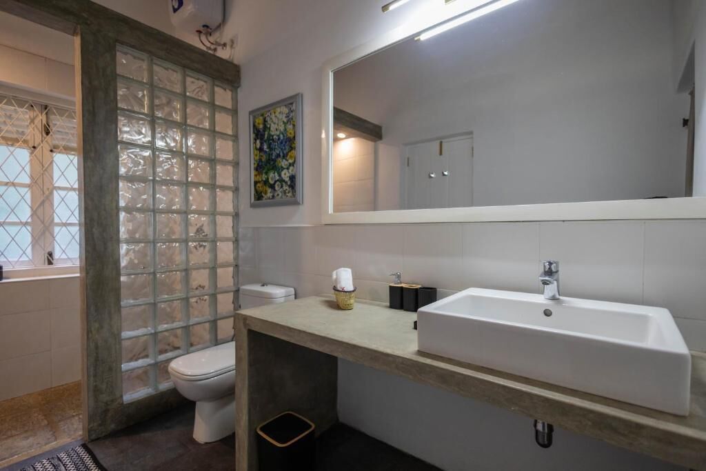 Un baño con inodoro, lavamanos, espejo y ventana con vidrio esmerilado.