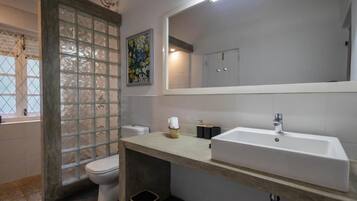 Un baño con inodoro, lavamanos, espejo y ventana con vidrio esmerilado.