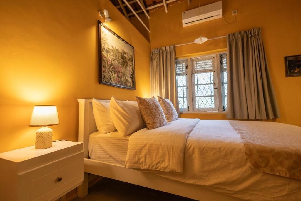 Un dormitorio con una cama, una mesita de noche, una lámpara, una ventana con cortinas y un equipo de aire acondicionado.