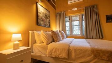Un dormitorio con una cama, una mesita de noche, una lámpara, una ventana con cortinas y un equipo de aire acondicionado.