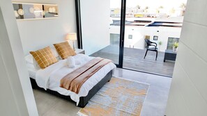 A hotel room with a bed, a small table, a chair, and a view of the cityscape. -  Silver Sands Beach Villa (Langstrand)