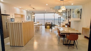 Una cocina moderna con vistas al mar, un comedor con una mesa grande y una zona de estar acogedora.