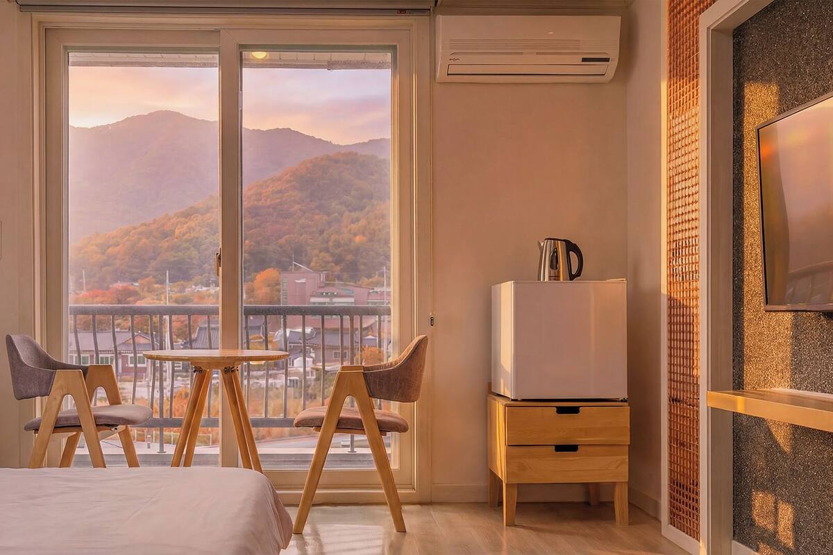 Une chambre d’hôtel avec un balcon, un lit, une petite table avec des chaises, un réfrigérateur et un téléviseur fixé au mur.