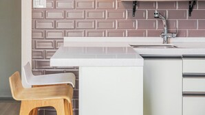 Una cocina con mostrador blanco, una silla de madera y un salpicadero de azulejos.