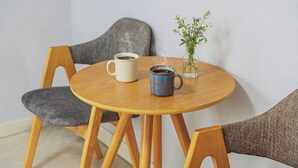 Una mesa redonda de madera con dos tazas de cerámica y un florero de vidrio con flores.