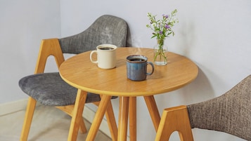 A round wooden table with two ceramic mugs and a glass vase with flowers.