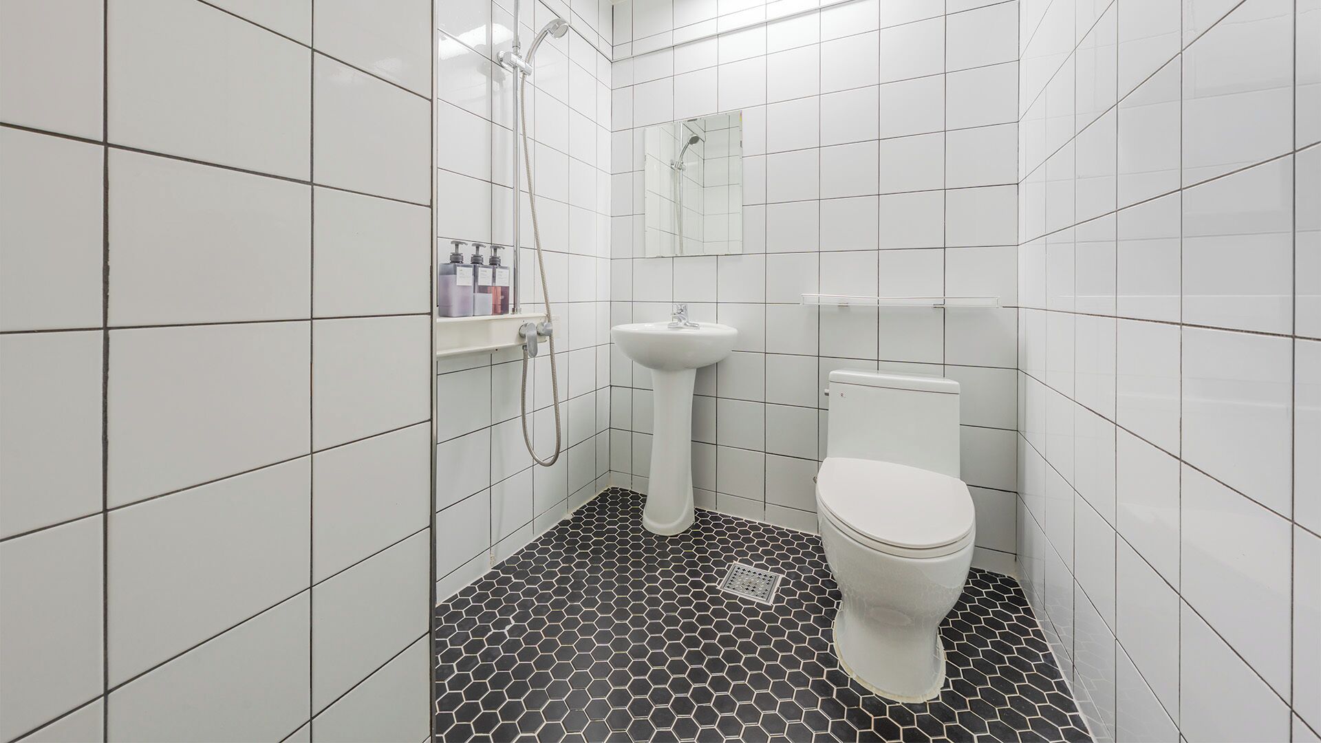 A bathroom with white tiled walls, a white pedestal sink, a toilet, and a shower with a glass enclosure.