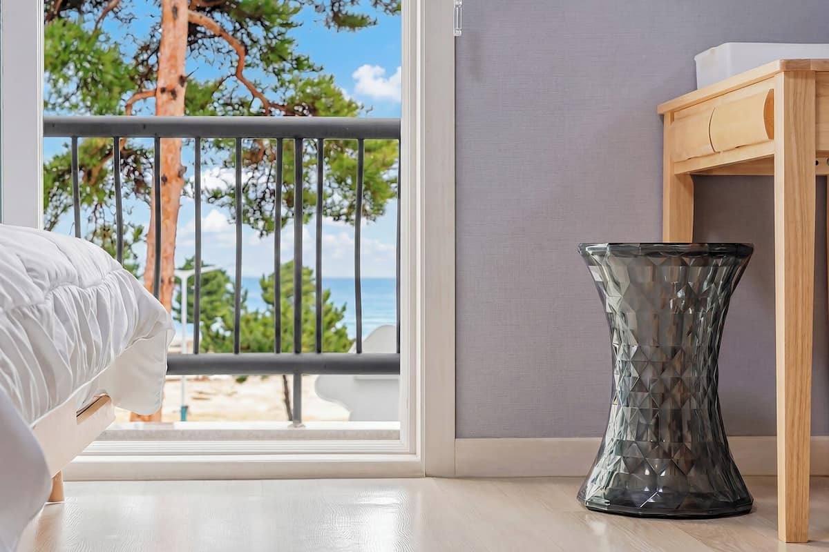 Une chambre avec un lit, un vase en verre et une vue sur la plage depuis un balcon.