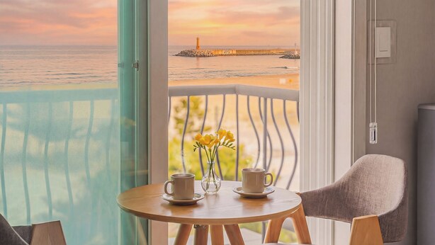 Un balcón con vista al mar, una mesa con dos tazas y un florero, y una silla.