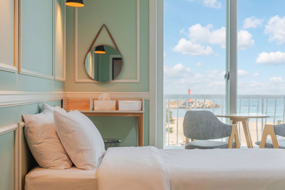 Une chambre d’hôtel avec un lit, une table de chevet, un miroir et une vue sur la mer.