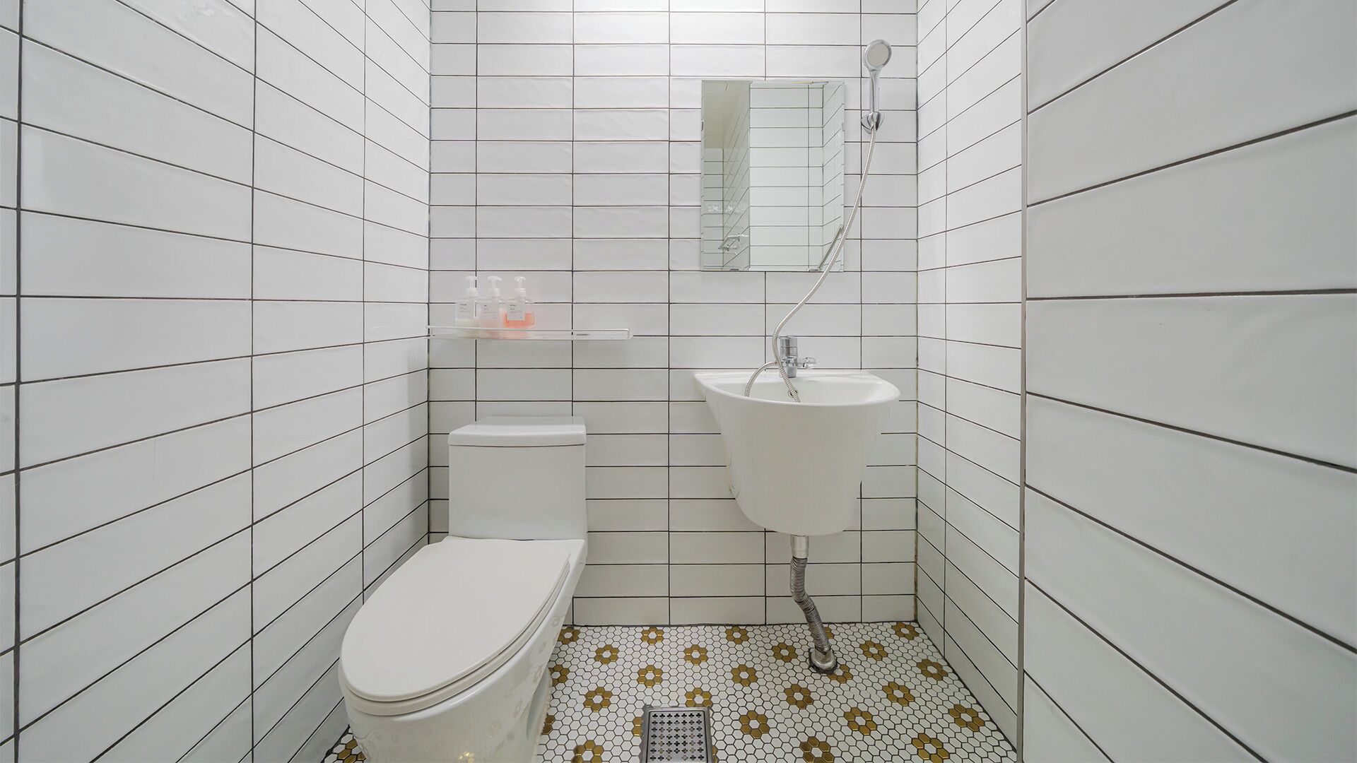 A small bathroom with white tiled walls, a toilet, a sink, and a shower.