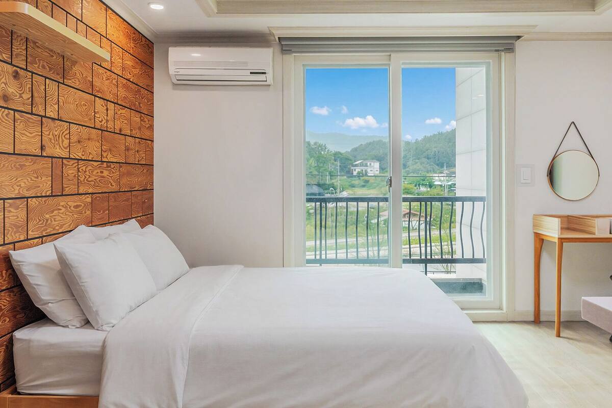 Une chambre avec un lit, un mur en bois, un balcon avec vue et une petite table avec un miroir.
