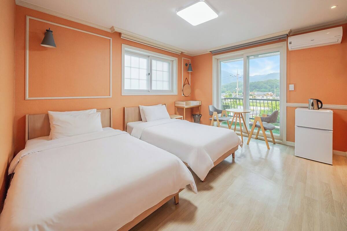 Une chambre d’hôtel avec deux lits, une petite table, une chaise, un réfrigérateur et un balcon avec vue.
