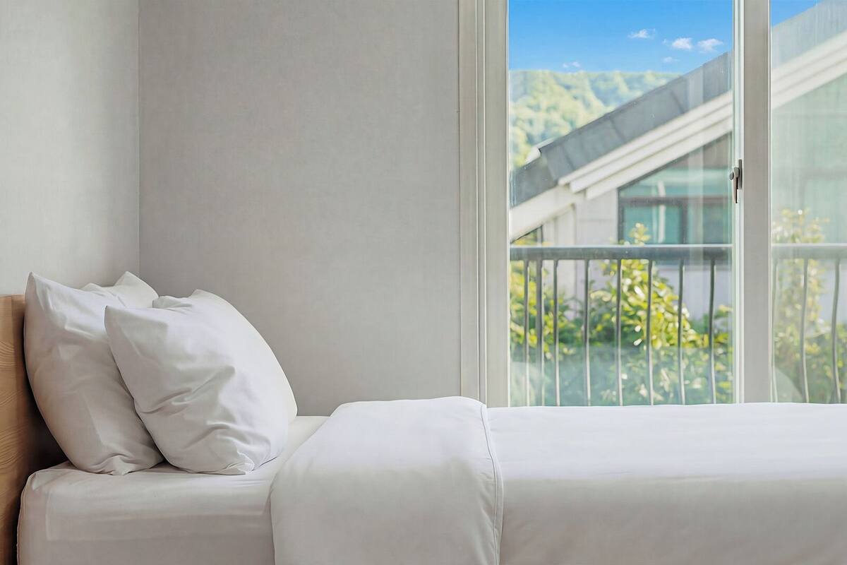 Une chambre à coucher avec un lit, des oreillers et une vue sur un immeuble par la fenêtre.