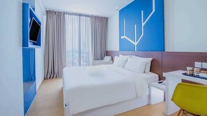 Une chambre d’hôtel moderne, dotée d’un grand lit, d’un bureau, d’une chaise et d’un téléviseur fixé au mur.