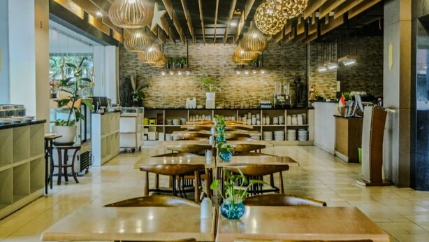 Un restaurant spacieux avec des tables en bois et des lampes suspendues, un mur en pierre et un coin bar.