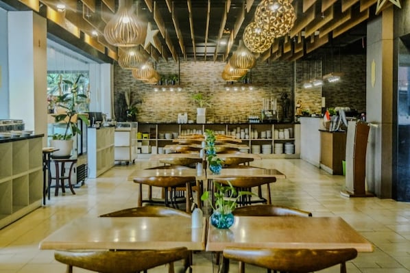 A spacious restaurant with wooden tables and hanging pendant lights, a stone wall, and a bar area.