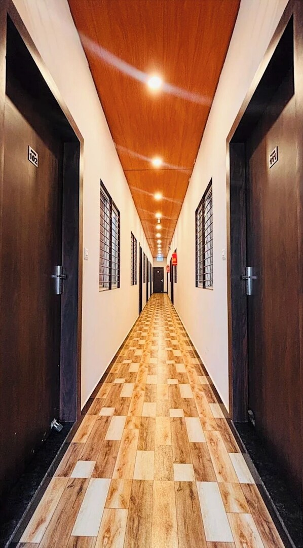 Un couloir d’hôtel avec un plancher en bois, des portes sombres et un plafond en bois.