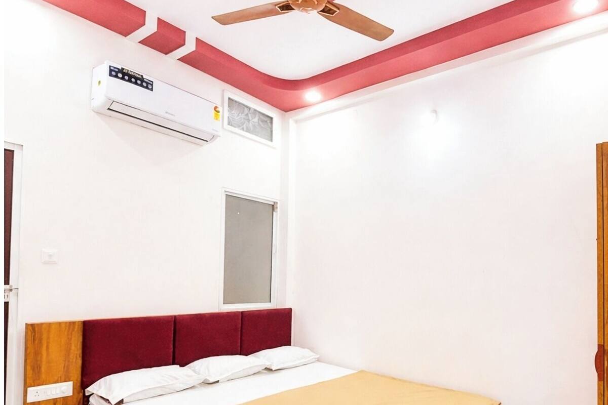 Un dormitorio con una cama de madera, un ventilador de techo, un equipo de aire acondicionado, una mesita de noche y una alfombra.