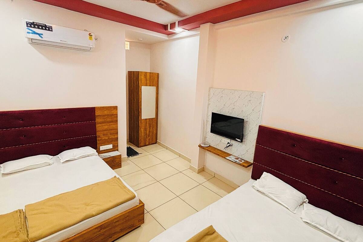 Habitación de hotel con dos camas, televisor, aire acondicionado y puerta de madera.