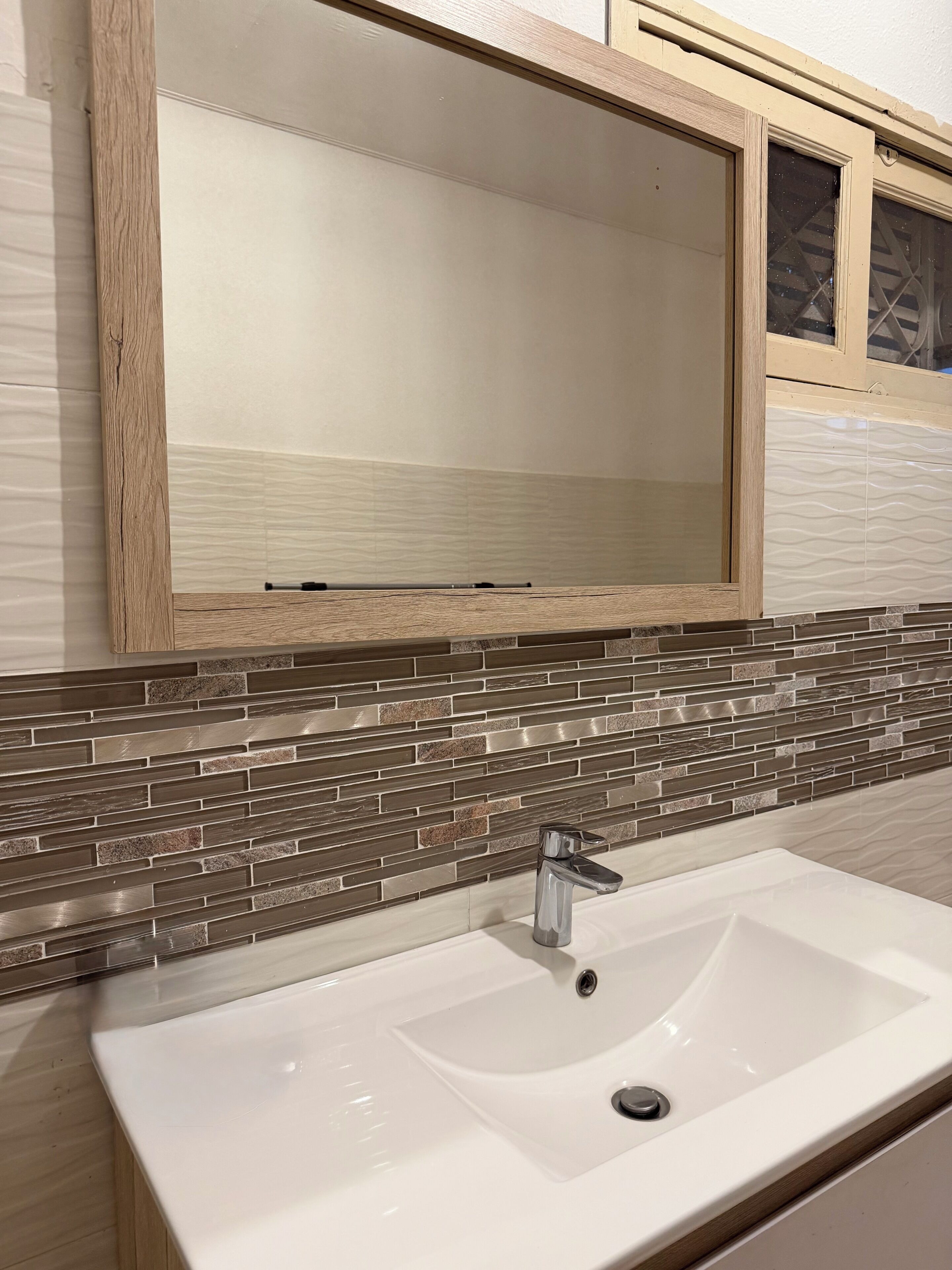 A bathroom with a white sink, a wooden-framed mirror, and a tiled backsplash.