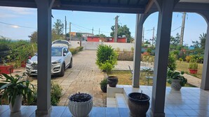 A covered patio with a car parked outside, potted plants, and a view of a residential area.
