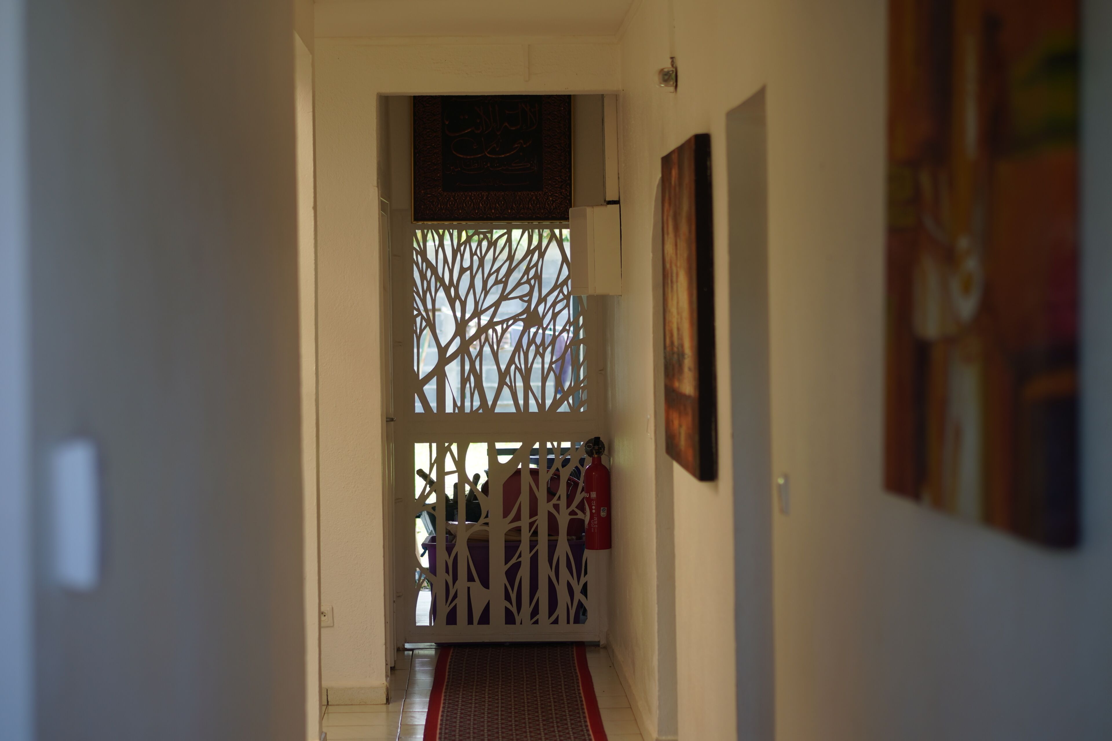 A hallway with a decorative screen, a fire extinguisher, and artwork on the walls.