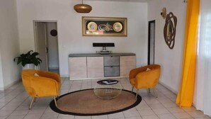 A living room with two yellow armchairs, a round coffee table, a television on a cabinet, and a potted plant.