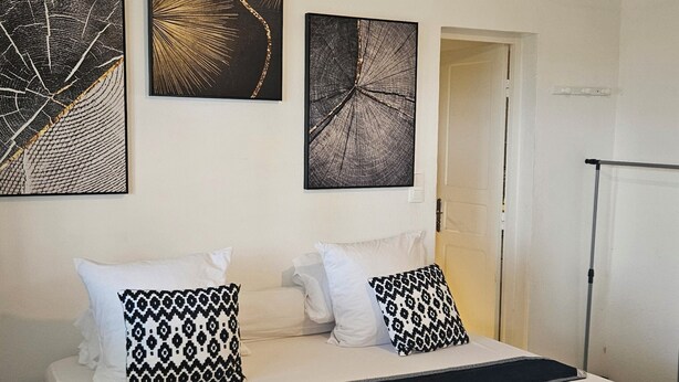 A bedroom with a bed, two nightstands, a hanging light fixture, and three wall-mounted artworks.