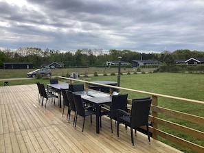 Eine Holzterrasse mit Gartenmöbeln, Blick auf eine Rasenfläche und Häuser im Hintergrund.