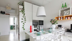 A modern kitchen with white cabinetry, a central island with bar stools, a hanging light fixture, and a clock on the wall. - De Angeli 60-square-meter apartment - M1 & M4 - near CityLife, Tortona district, San Siro (Milano)