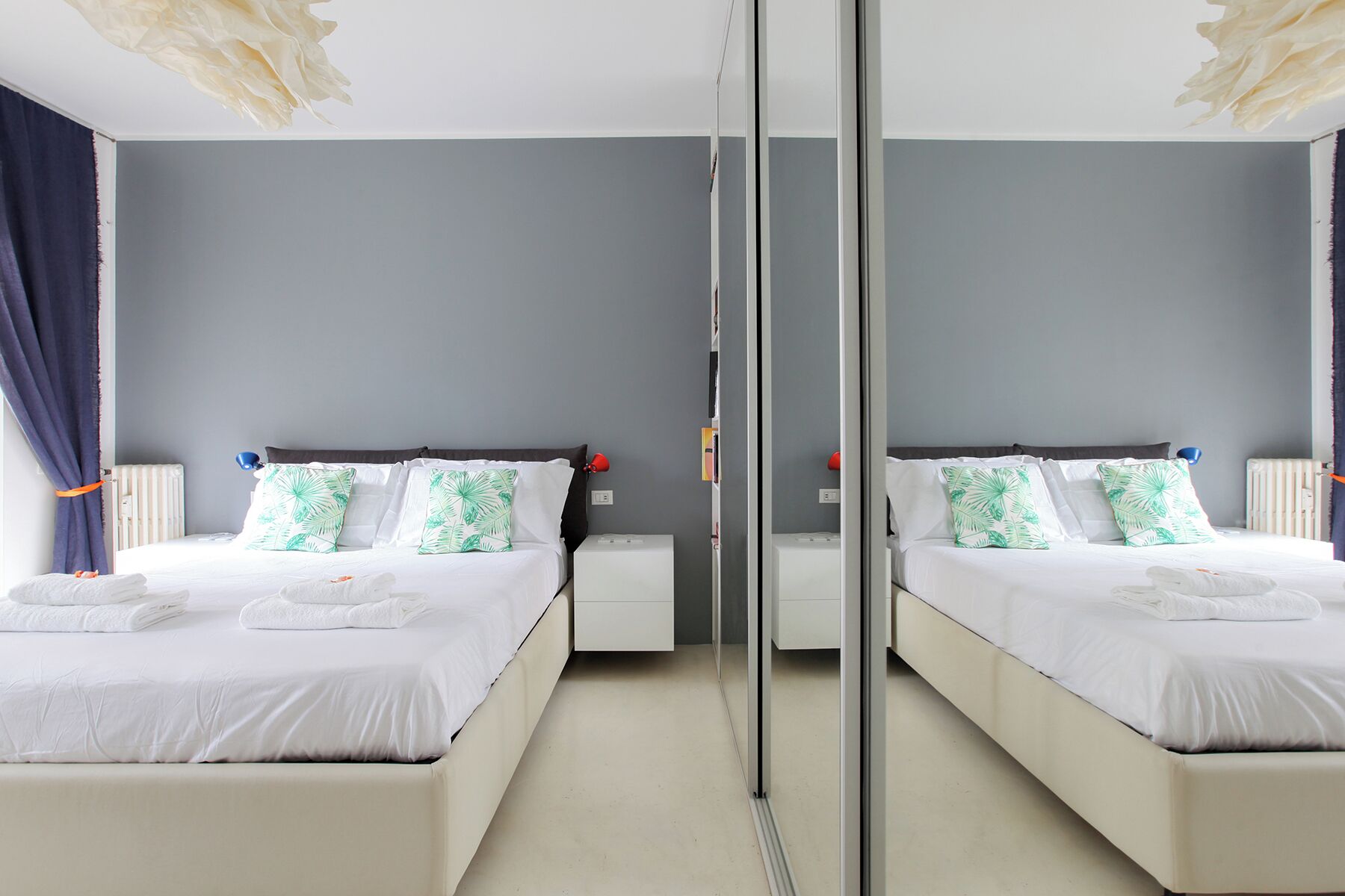 Habitación con espejos, dos camas, ropa de cama blanca y almohadas con estampado de hojas tropicales.