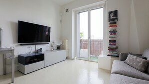 A living room with a flat-screen TV, a bookshelf, a sofa, and a sliding glass door leading to an outdoor area. - De Angeli 60-square-meter apartment - M1 & M4 - near CityLife, Tortona district, San Siro (Milano)