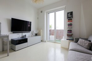 A living room with a flat-screen TV, a bookshelf, a sofa, and a sliding glass door leading to an outdoor area. - De Angeli 60-square-meter apartment - M1 & M4 - near CityLife, Tortona district, San Siro (Milano)