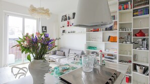 A modern kitchen with a dining table, a white vase with flowers, and a bookshelf filled with books and kitchenware. - De Angeli 60-square-meter apartment - M1 & M4 - near CityLife, Tortona district, San Siro (Milano)