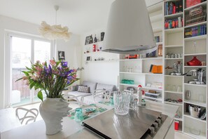 A modern kitchen with a dining table, a white vase with flowers, and a bookshelf filled with books and kitchenware. - De Angeli 60-square-meter apartment - M1 & M4 - near CityLife, Tortona district, San Siro (Milano)