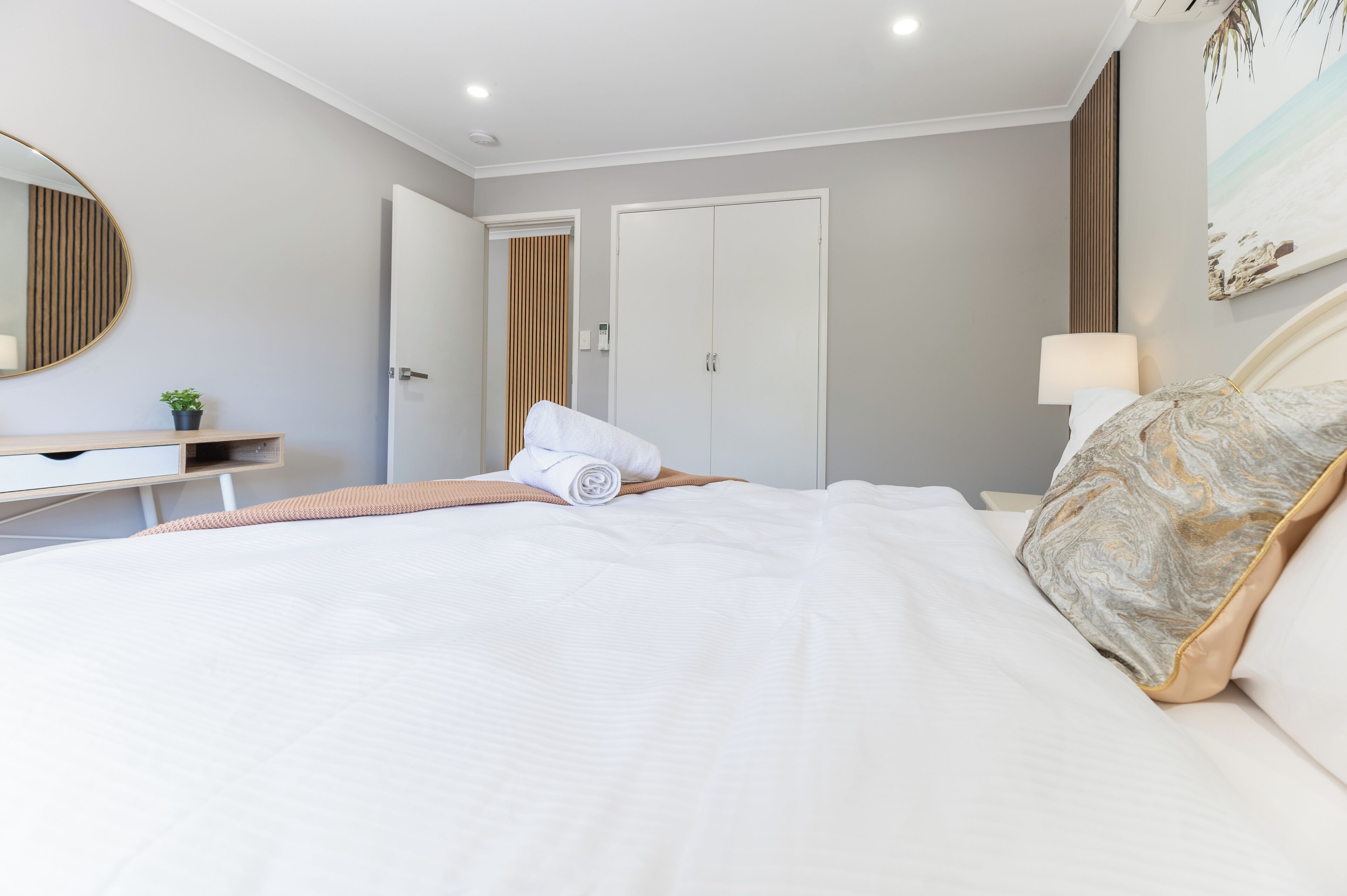 A bedroom with a bed, a bedside table, a mirror, a door, and a wall-mounted lamp.