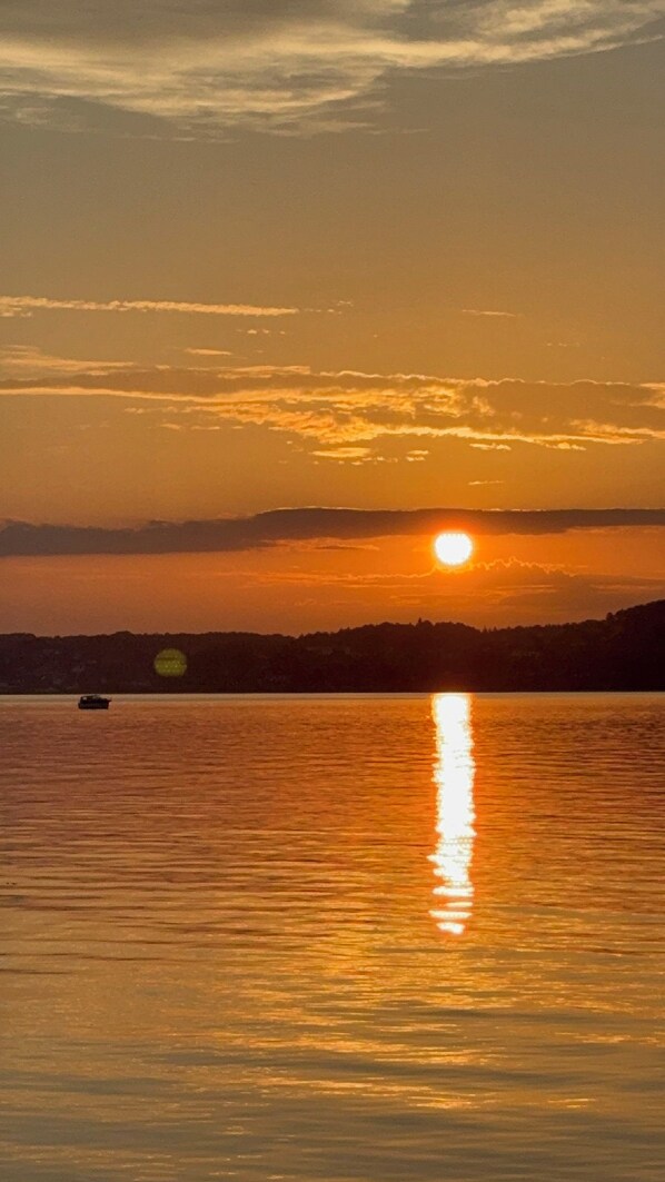 A sunset over a calm body of water with a boat and a distant shoreline.