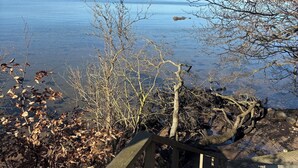 A wooden deck leading to a lake with clear water, surrounded by bare trees and a distant shoreline. - Fully modernized in 2026, 1 minut from the ocean (Børkop)