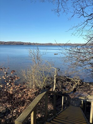 A wooden deck leading to a lake with clear water, surrounded by bare trees and a distant shoreline. - Fully modernized in 2026, 1 minut from the ocean (Børkop)