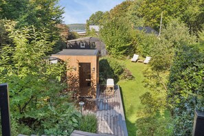 A wooden deck with a small building, a grassy yard, and a view of a lake.