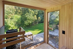 A wooden deck with a bench and a fire pit, overlooking a lush green garden.
