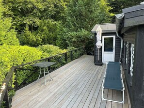 Une terrasse en bois avec une petite table et une chaise, entourée d’une végétation luxuriante.