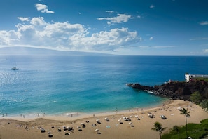 Una playa con aguas azules cristalinas, un litoral rocoso y un edificio blanco con balcón.