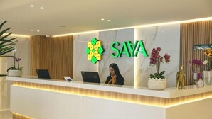 A reception desk with a logo, a receptionist, and a plant. - Saya Hotel & Suites (Sayausi)