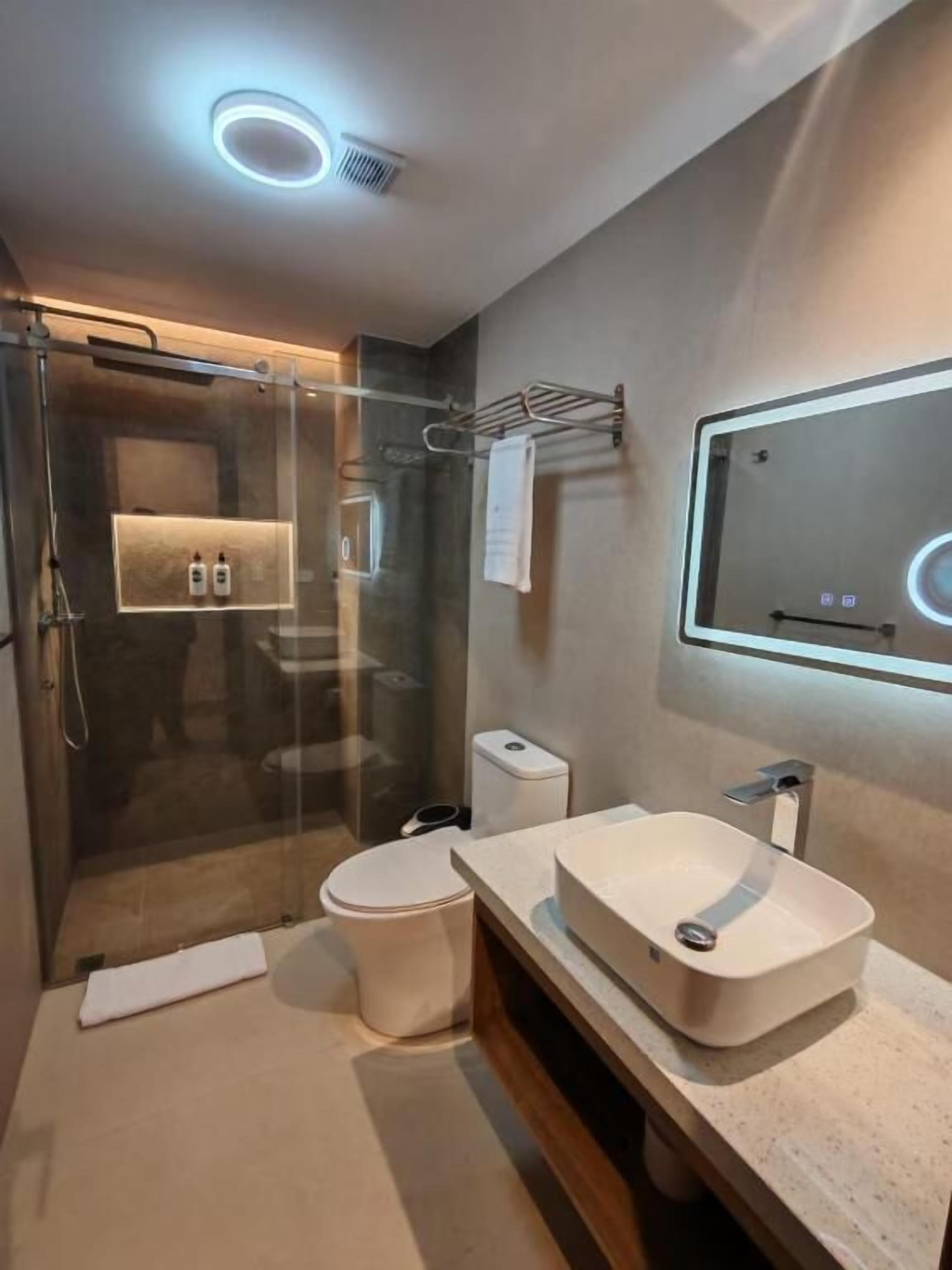 Un baño moderno con ducha de vidrio, inodoro, lavabo con espejo y toallero.