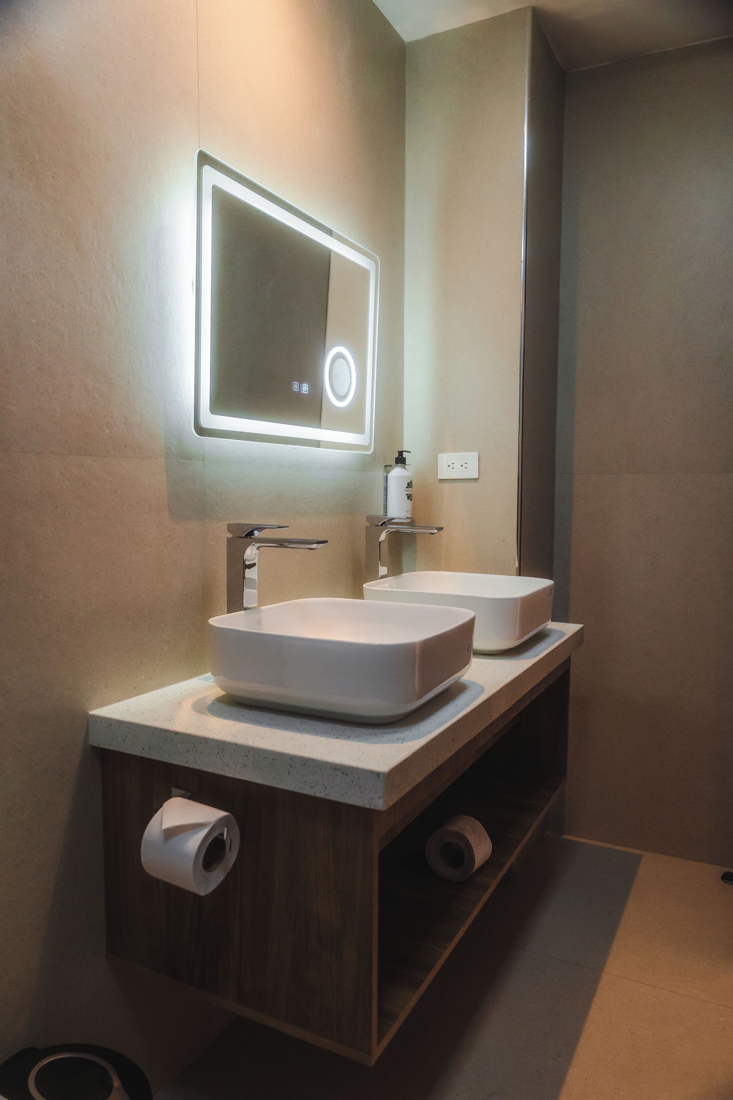 Un baño moderno con dos lavamanos, un espejo y un dispensador de papel higiénico.