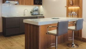 A modern kitchen with wooden cabinets, a central island, bar stools, and a microwave. - Saya Hotel & Suites (Sayausi)