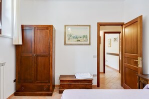 A bedroom with a bed, wooden wardrobe, a painting on the wall, and a hallway leading to another room. - Majestic Villa Retreat (Assisi)
